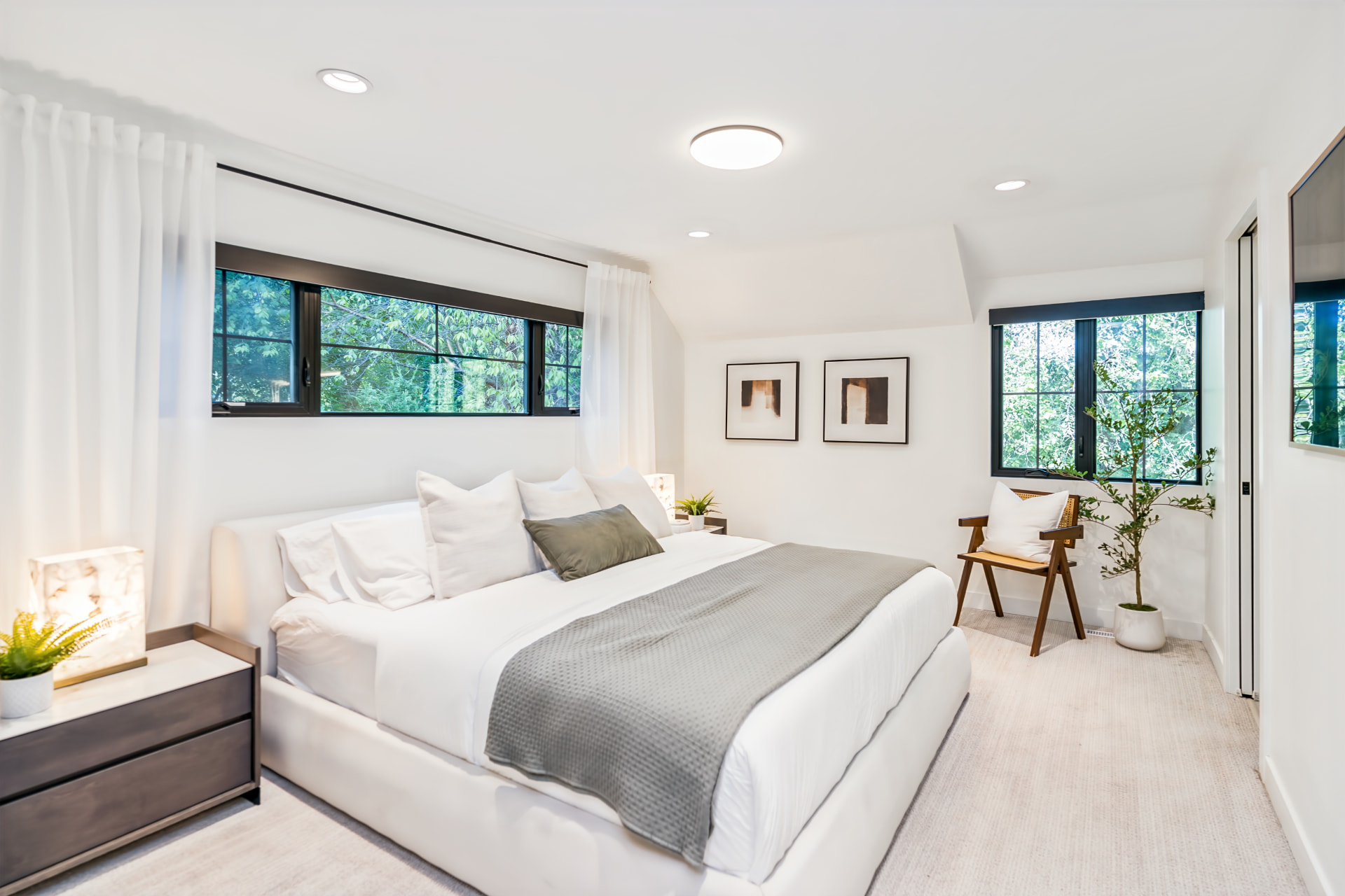 Primary bedroom with black-framed windows overlooking the Red River and mature trees